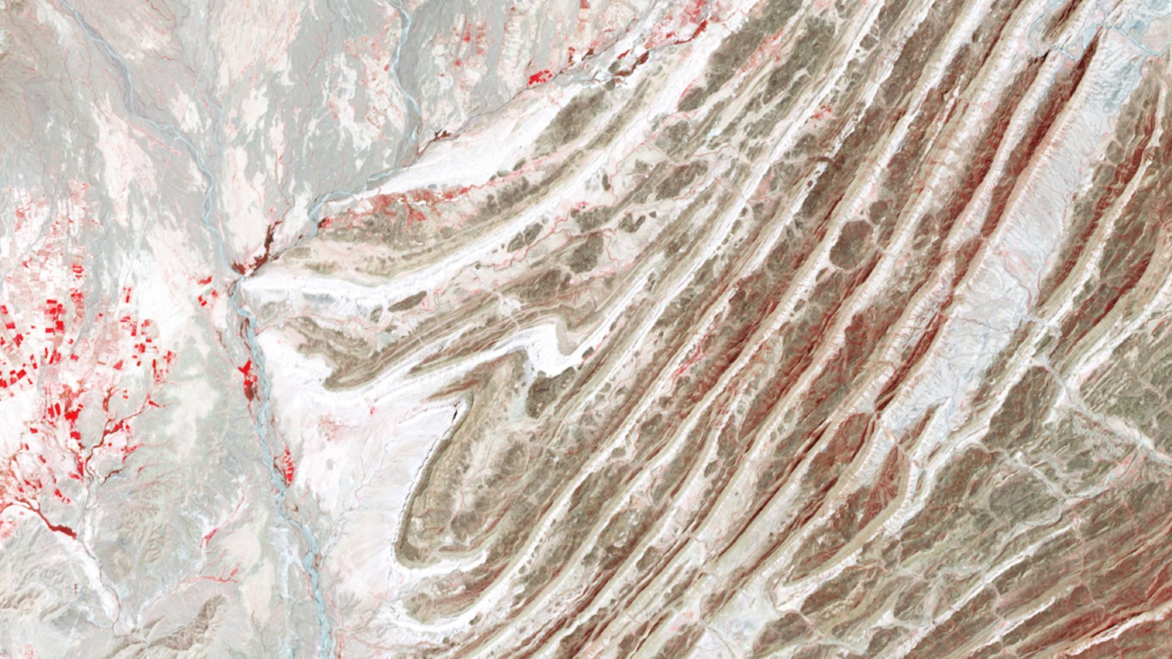 A false-color satellite photo of a series of alternating rocky folds across the landscape
