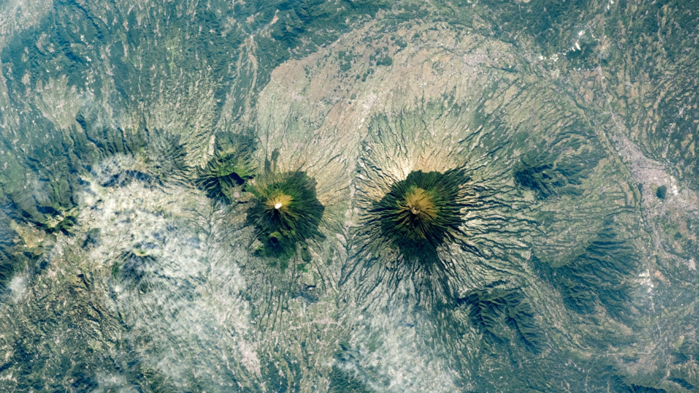 An astronaut photo of two near-identical volcanoes standing side-by-side on Indonesia's Java Island.